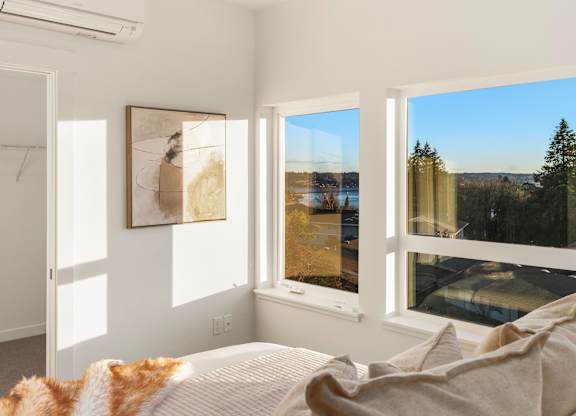 A bedroom with a large bed and a view of the outdoors through the windows at The Narrows at Clare Apartments , Apartments, Bremerton, WA