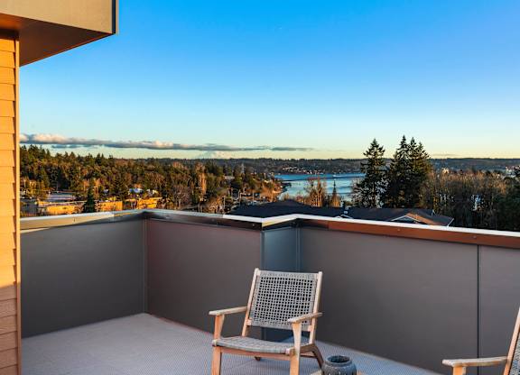 Two chairs are on a balcony overlooking a body of water and trees at The Narrows at Clare Apartments , Bremerton