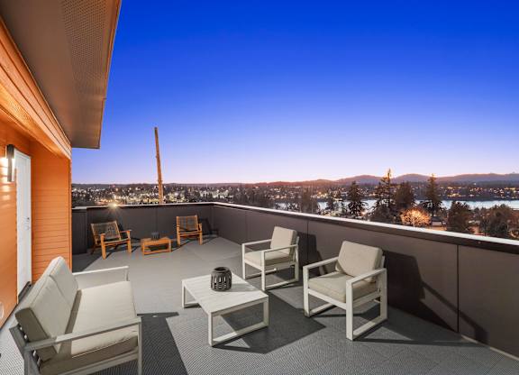 A balcony with white chairs and a table overlooking a cityscape at dusk at The Narrows at Clare Apartments , Washington