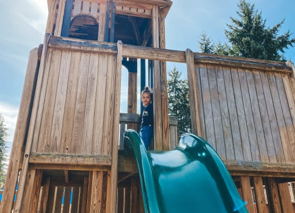 a young boy stands in the doorway of a wooden playset with a slide at Rivulet, Silverdale, 98383