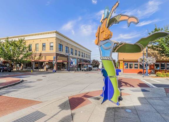 A large, colorful sculpture of a bird is situated in the middle of a city square.