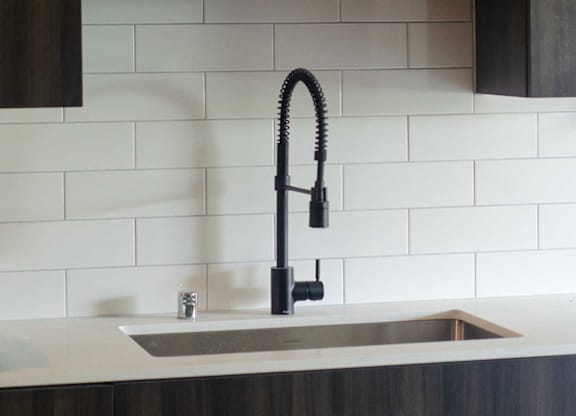 A modern kitchen with a white sink and black faucet at B Flats Apartments, Bremerton, WA, 98337