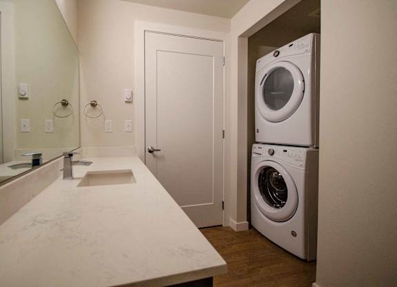 A white bathroom with a sink, mirror, and washer and dryer at B Flats Apartments, Bremerton, WA