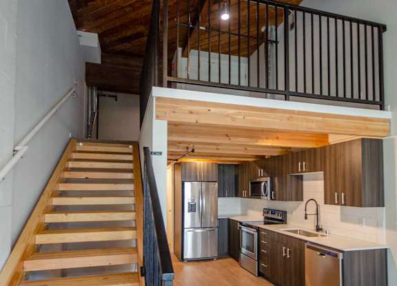 A wooden staircase with a metal railing leads to a kitchen area at B Flats Apartments, Washington