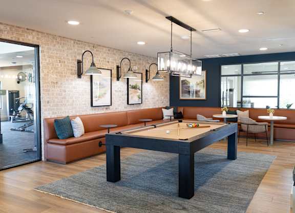 A billiard table is in the middle of a room with a brick wall and a mirror. at The Crest at Oakwood Apartments, Oakwood , GA, 30566