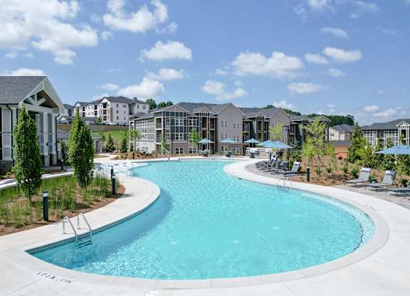 A large outdoor swimming pool surrounded by lounge chairs and umbrellas. at The Crest at Oakwood Apartments, Georgia
