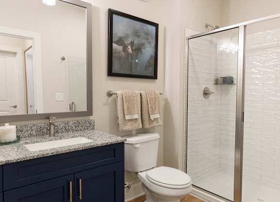Secondary bathroom with a glass-encoder shower and navy vanity in a two-bedroom apartment at The Crest at Oakwood in Oakwood, GA.