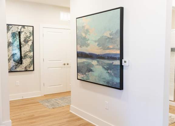 Hallway with wood-look flooring and frames artwork in a two-bedroom model apartment at The Crest at Oakwood in Oakwood, GA.