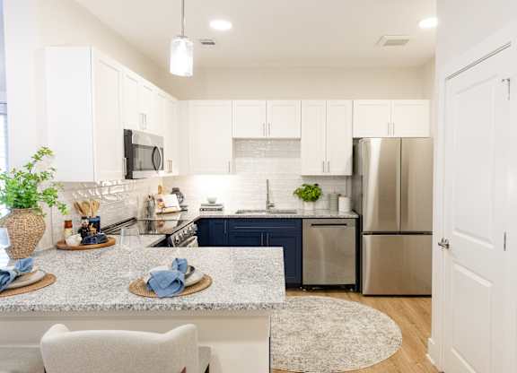 Kitchen with stainless steel appliances, white cabinetry and breakfast bar at The Crest at Oakwood apartments in Oakwood, GA.