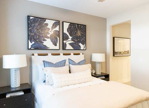 Primary bedroom with a staged bed, bedside tables and framed artwork in a two-bedroom model apartment at The Crest at Oakwood in Oakwood, GA.