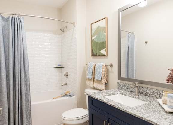 Main bathroom with a tub-shower combination and navy vanity in a two-bedroom apartment at The Crest at Oakwood in Oakwood, GA.