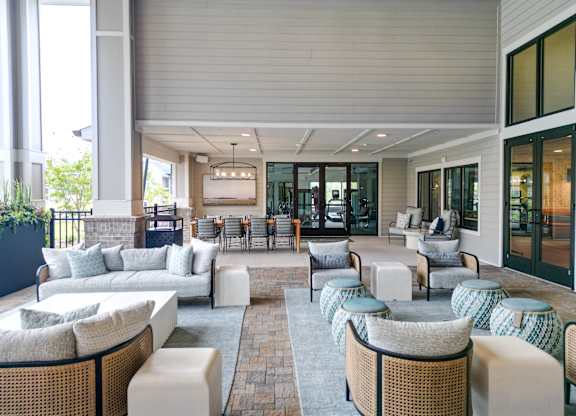 Covered outdoor clubhouse seating area with sofas and lounge chairs at The Crest at Oakwood apartments in Oakwood, GA.