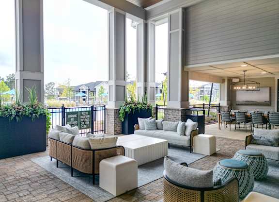 Outdoor clubhouse lounge with sofas, planters and tall covered columns at The Crest at Oakwood apartments in Oakwood, Ga.