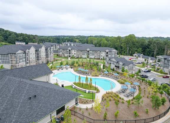Aerial view of the swimming pool, landscapes grounds and surrounding apartment buildings at The Crest at Oakwood in Oakwood, GA.