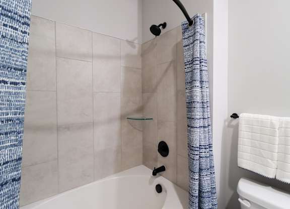 Bathtub with glass shelf and black fixtures at The Crest at South Point Apartments, McDonough, 30253