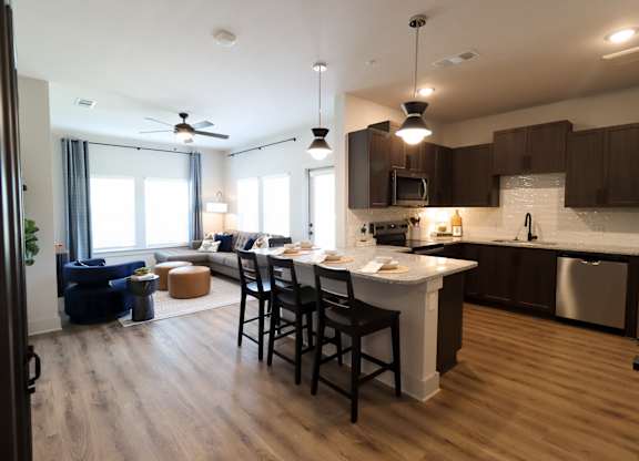 Open concept living area with kitchen island and pendant lighting at The Crest at South Point Apartments, McDonough, GA
