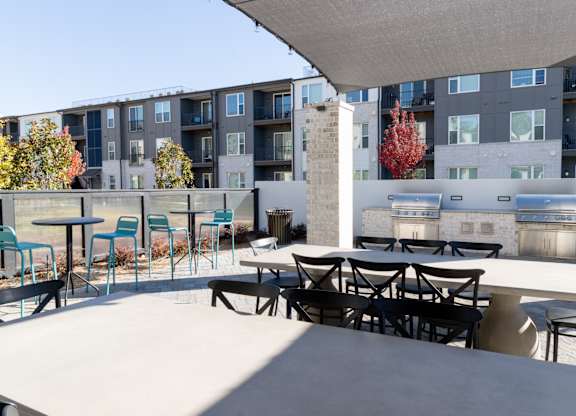 Outdoor grilling area with dining tables and shade canopy at The Wren Apartments, Georgia, 30043