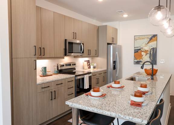 Modern kitchen with granite countertop and light wood cabinets at The Wren Apartments, Lawrenceville, GA
