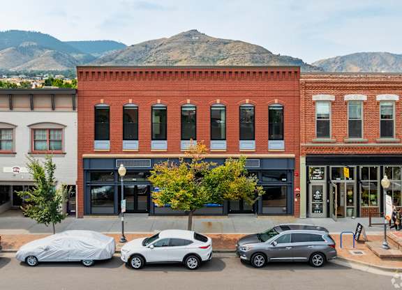 Cars parked in front of a red brick building with a mountain in the background.
