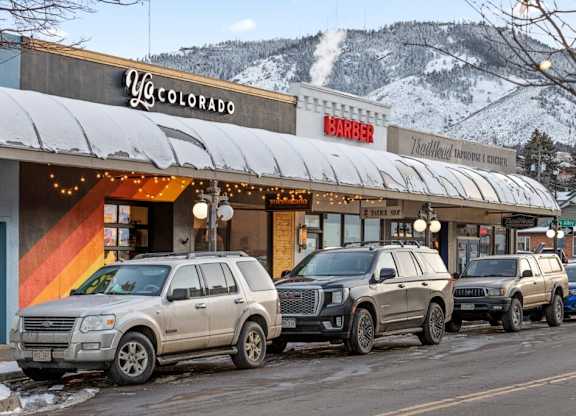 A row of SUVs are parked in front of a barber shop and a yoga studio at The Avenue Lofts Golden Apartments, Colorado, 80401