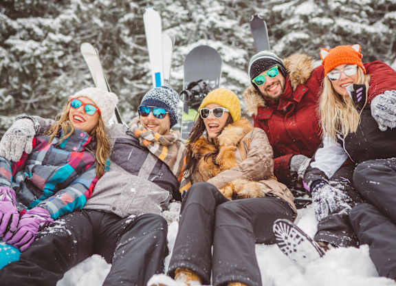 A group of friends are sitting in the snow with their skis and snowboards.