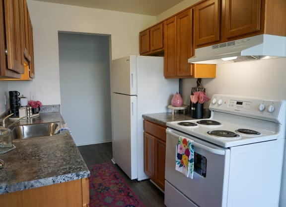 Kitchen with granite countertop, oven, refrigerator, sink, and wood cabinets, at Gale Gardens Apartments,