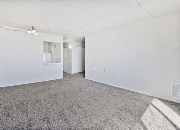 A large empty room with a carpeted floor and a small mirror on the wall.