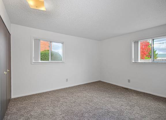 A room with a carpeted floor and two windows.