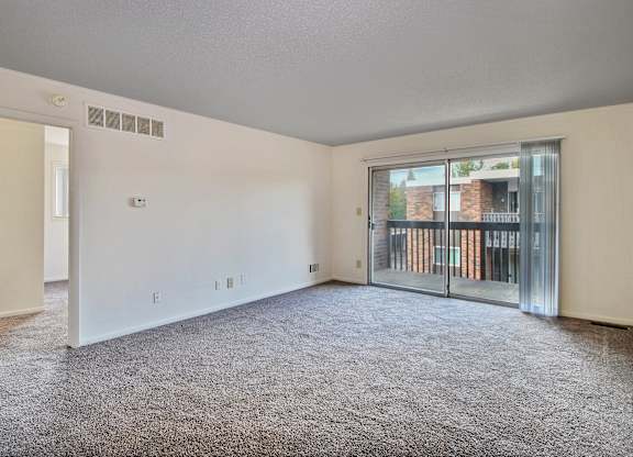A spacious room with a grey carpet and a sliding glass door leading to a balcony.
