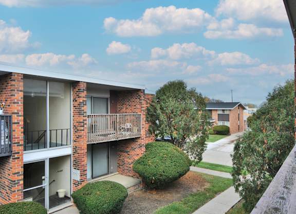 A balcony of a brick building overlooks a green lawn and other buildings.