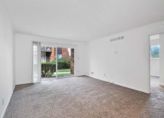 A large empty room with a carpeted floor and a sliding glass door leading to a backyard.