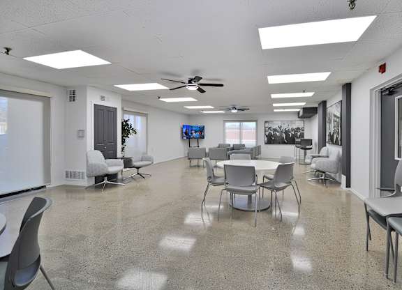 A room with a white ceiling and a grey floor with chairs and tables.