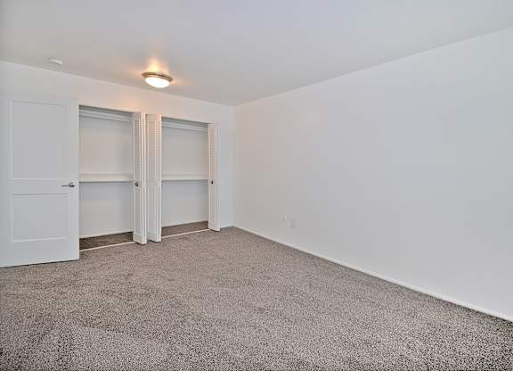 Comfortable bedroom at Woodcrest Apartments in Westland, MI featuring soft carpet flooring, a large closet, and peaceful natural light.