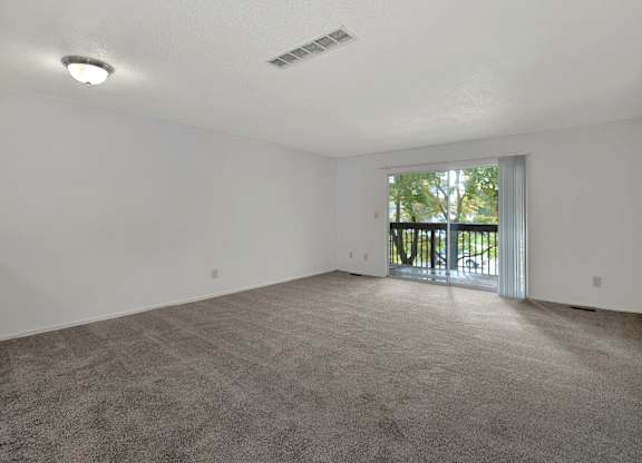 A spacious room with a grey carpet and a sliding glass door leading to a balcony.