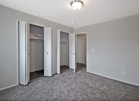 Bright bedroom with large closet, neutral paint, and soft carpeting at Warren Woods Apartments in Warren, MI.