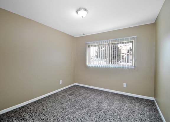 Comfortable bedroom at Woodcrest Apartments in Westland, MI featuring soft carpet flooring, a large closet, and peaceful natural light.