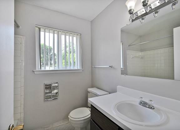 Bathroom with white vanity, framed mirror, and shower-tub combo at Warren Woods Apartments in Warren, MI.