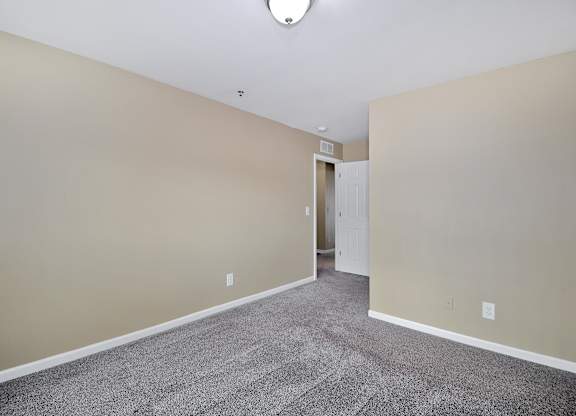Comfortable bedroom at Woodcrest Apartments in Westland, MI featuring soft carpet flooring, a large closet, and peaceful natural light.