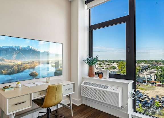 A room with a desk, chair, and a large window with a view of a cityscape.
