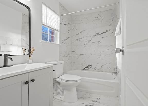 A white bathroom with marble tiles on the walls.