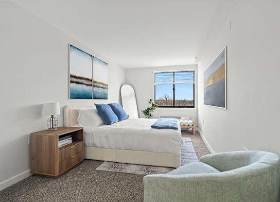 A bedroom with a bed, a chair, and two pictures on the wall.
