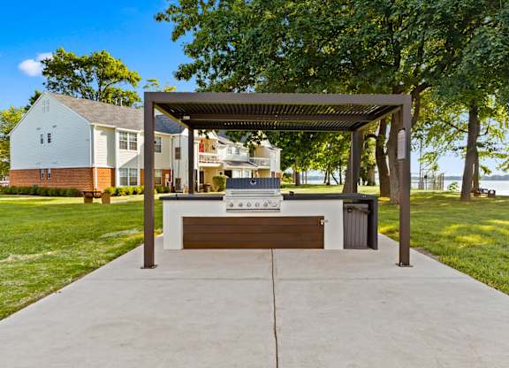 A pavement leads to a pavilion with a bench and a table underneath it.