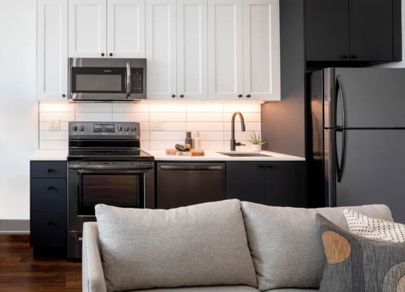 a living room with a couch and a kitchen with black appliances at The Irvine, Pennsylvania