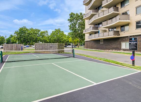 A tennis court is surrounded by a fence and a building at Premier at Cherry Hill, New Jersey