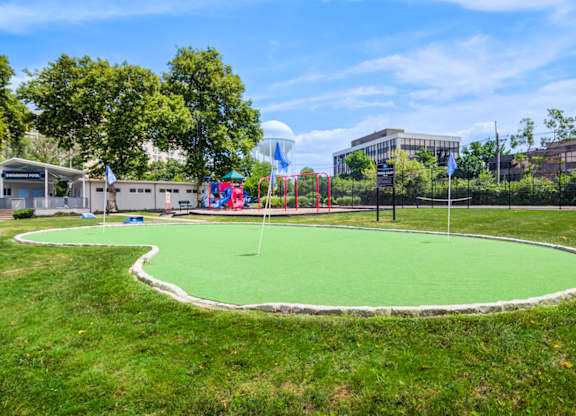 A green artificial turf in the foreground with a playground and buildings in the background at Premier at Cherry Hill, Cherry Hill