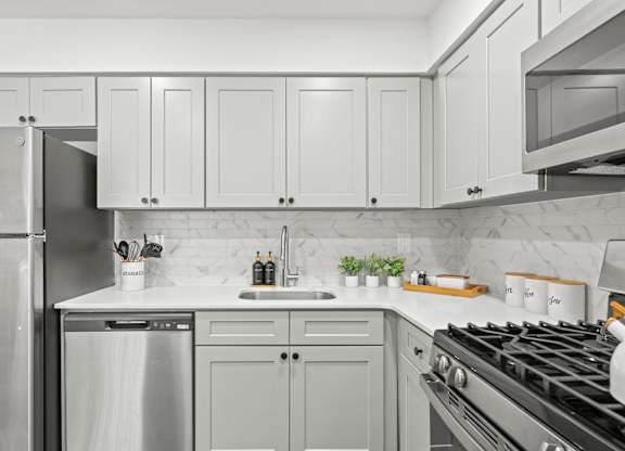A modern kitchen with a stainless steel refrigerator, a white countertop, and a black stove top.