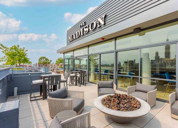 A patio area with a fire pit and chairs in front of a building with a sign that says