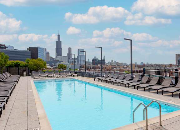 A swimming pool with lounge chairs and a city skyline in the background.