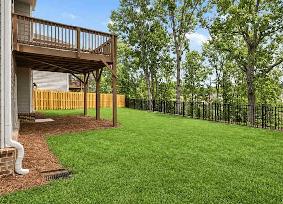 A backyard with a wooden deck and a black fence.