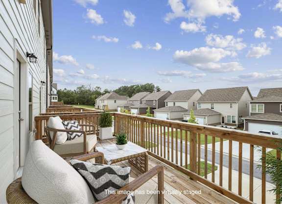 A balcony with a white couch and pillows overlooks a residential street.